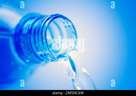 gros plan de l'eau qui coule de la bouteille sur fond bleu Banque D'Images