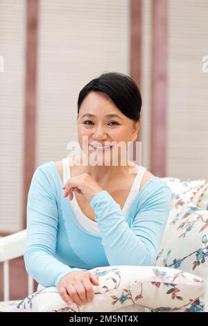 Bonne femme d'âge moyen assise sur le canapé Banque D'Images
