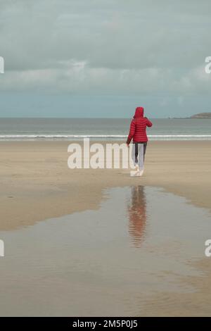 Une femme rouge marchant sur une plage froide en bretagne Banque D'Images