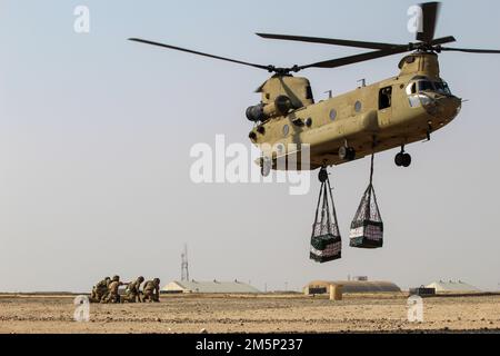 Soldats américains avec la Compagnie de camion composite 1067th, 228th Bataillon de transport automobile, 213th Groupe de soutien régional, Garde nationale de l'Armée de Pennsylvanie, 389th Bataillon de soutien au combat, 77th Brigade de soutien, Et un soldat britannique affecté à la Brigade aérienne de combat de 16 regarde un CH-47 Chinook se retirer lors d'un exercice d'entraînement au Camp Buehring, au Koweït, le 26 février 2022. Les soldats s'étaient formés dans le cadre de la Force opérationnelle interarmées combinée – opération détermination inhérente pour conseiller, aider et permettre aux forces en partenariat de vaincre durablement Daesh à l'intérieur Banque D'Images