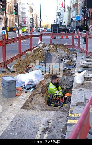 Workman regardant le téléphone mobile tout en travaillant dans des travaux de roadworks trou creusé à Fleet Street Londres Angleterre Royaume-Uni 2022 KATHY DEWITT Banque D'Images