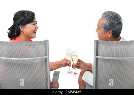 Un couple de personnes âgées heureux assis sur une chaise de plage boit du champagne Banque D'Images