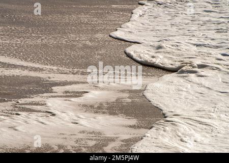 De douces vagues océaniques se jettent sur le littoral sablonneux de Praia da Cresmina près de Guincho, au Portugal, créant des motifs d'écume marine sous la lumière douce du soleil. Banque D'Images