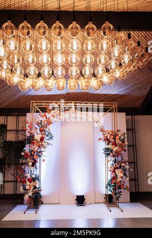 Magnifique mariage or métal arc, mur, zone de photo, zone décorée avec des fleurs lumineuses et des verts dans le hall pour la cérémonie de mariage. Décor festif au banq Banque D'Images