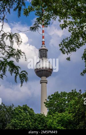 Berlin, Allemagne - 25 juin 2022: La célèbre tour de télévision (Fernsehturm) sur Alexanderplatz, encadrée par des branches d'arbres verts Banque D'Images