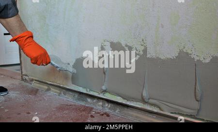 mortier plastique appliqué sur un mur de pièce en couches épaisses pour niveler la surface, le plâtrier applique le mortier sur la texture du mur à l'aide d'une spatule Banque D'Images