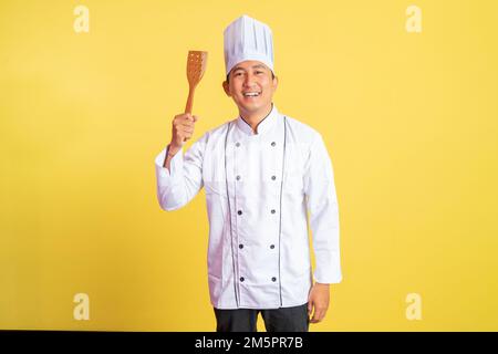 un chef cuisinier excités portant une veste de chef tenant une spatule Banque D'Images