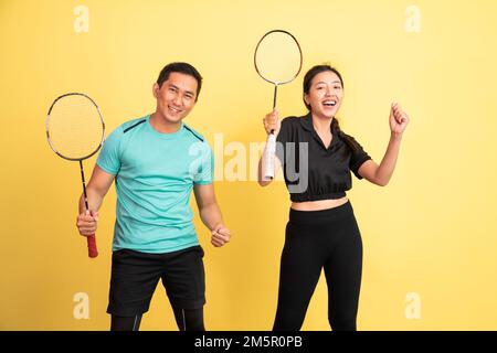 des femmes et des hommes enthousiastes tenant des raquettes sur fond jaune Banque D'Images