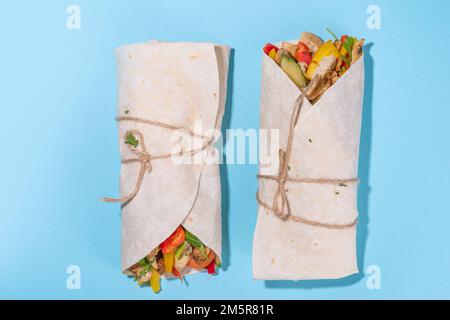 Classique rue nourriture shawarma ou burrito, sandwich sain enveloppé dans la tortilla pain plat avec viande de poulet frite, légumes frais, sauce, sur b vif Banque D'Images