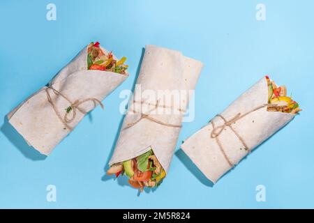 Classique rue nourriture shawarma ou burrito, sandwich sain enveloppé dans la tortilla pain plat avec viande de poulet frite, légumes frais, sauce, sur b vif Banque D'Images