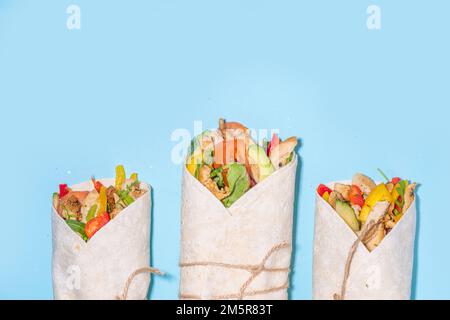 Classique rue nourriture shawarma ou burrito, sandwich sain enveloppé dans la tortilla pain plat avec viande de poulet frite, légumes frais, sauce, sur b vif Banque D'Images