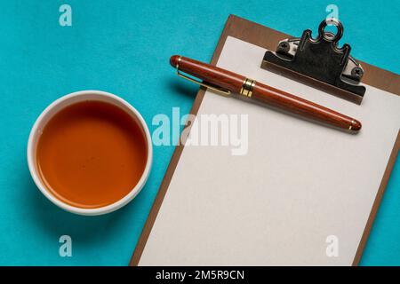 presse-papiers avec papier vierge, bureau plat avec une tasse de thé et un stylo élégant Banque D'Images