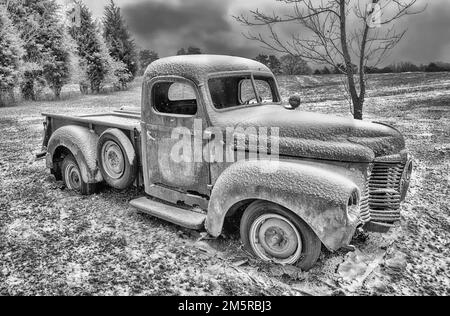 Une photo en noir et blanc d'un ancien pick-up IH de l'époque 1940s abandonné dans un champ enneigé. Banque D'Images