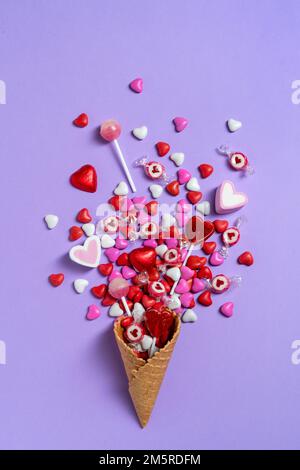 Cône gaufré sucré, bonbons, chocolats, sucettes, guimauve sur fond violet. Saint Valentin. Arrière-plan de vacances Banque D'Images