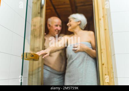 Un homme et une femme retraités âgés enveloppés de serviettes allant au sauna en bois du spa. Photo de haute qualité Banque D'Images