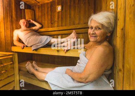 Homme et femme âgés enveloppés de serviettes de toilette se détendant dans le sauna en bois du spa. Photo de haute qualité Banque D'Images