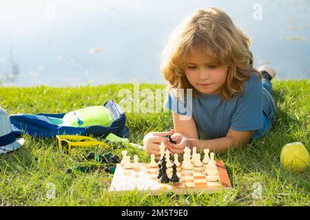 Gamin jouant au jeu d'échecs dans la cour arrière, en posant sur l'herbe. Échecs de jeu d'enfant concentré. Enfant jouant à un jeu de société en extérieur. Banque D'Images
