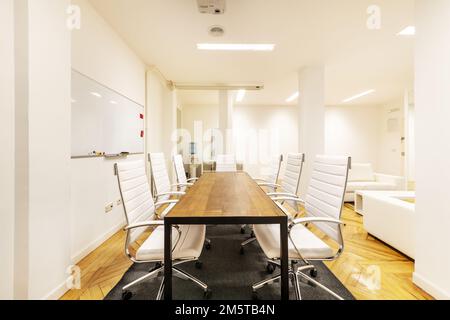 Table de bureau en bois avec cadre en métal et fauteuils pivotants rembourrés de skai blanc dans une salle de réunion avec canapés assortis Banque D'Images