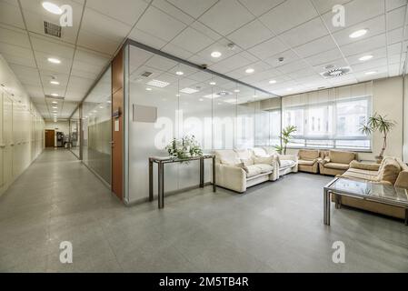 Couloir d'un immeuble de bureaux et bureaux séparés avec cloisons en verre, salles d'attente avec canapés et plafonds techniques Banque D'Images