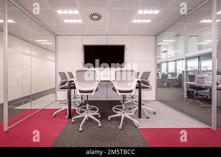 Table de réunion blanche avec chaises pivotantes assorties sur moquette multicolore dans un bureau en forme de bol à poisson avec cloisons en verre Banque D'Images