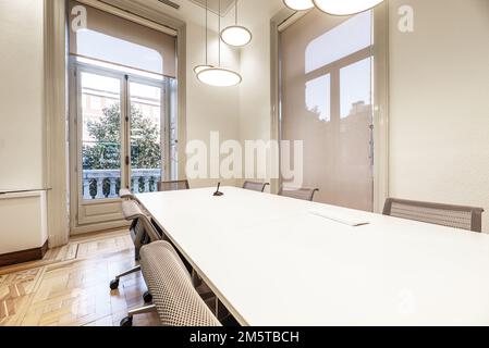 Salle de réunion d'un imposant bâtiment d'époque avec longue table blanche en bois et chaises pivotantes grises Banque D'Images