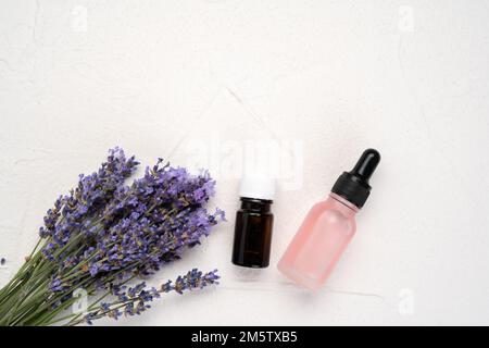 Bouteilles d'huile essentielle et fleurs de lavande sur fond blanc, vue de dessus, composition Flat Lay Banque D'Images