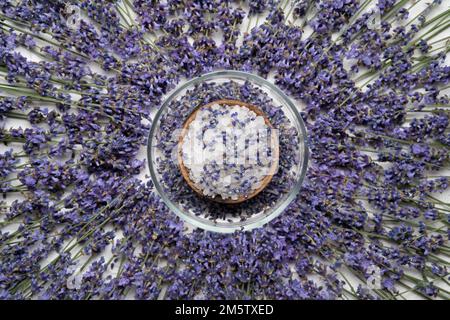 Sel de bain lavande dans un bol en bois et de nombreuses fleurs violettes sur fond blanc. Accessoires spa. Plan d'agencement, vue de dessus. Copier l'espace Banque D'Images