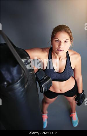 La différence entre essayer et triompher est ce petit umph. Portrait d'une boxeur femelle appuyé contre un sac de poinçonnage. Banque D'Images