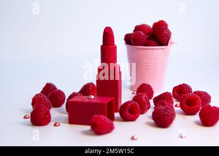 Rouge à lèvres brillant et framboises mûres juteuses sur fond blanc. Banque D'Images