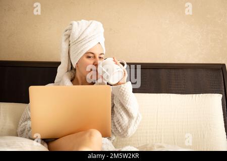 Après la douche, femme travaillant sur un ordinateur portable à la maison avec une tasse de café Banque D'Images