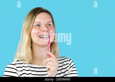 Jeune femme avec des bretelles dentaires se brossant les dents isolées sur fond bleu. Studio. Jolie petite fille, bretelles métalliques sur les dents blanches claires souriant. Banque D'Images