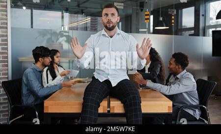 Homme fatigué dirigeant mâle patron société PDG homme d'affaires assis sur table bureau dans le bureau tenant les mains en avant geste stop viennent avec l'idée sur fond Banque D'Images