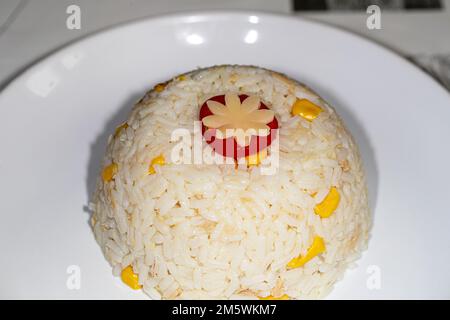 Portion de riz blanc servie sur une assiette, garnie de fleurs de légumes sculptées et de maïs. Repas simple. Banque D'Images