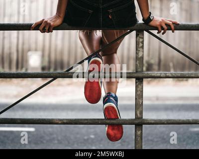 Le dos des jambes d'une fille repose sur une clôture en métal tout en portant des baskets montantes Nike Old-School. Banque D'Images