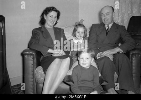 Années 1950, historique, photo de famille, une mère, un père et leurs deux jeunes enfants assis ensemble sur un petit canapé, souriant pour leur photo, Angleterre, Royaume-Uni. Banque D'Images