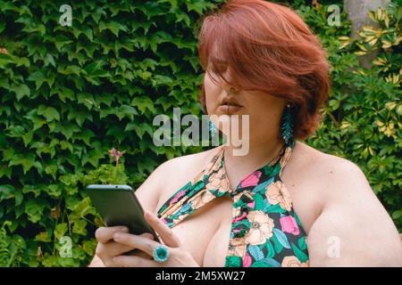 jeune femme du caucase du sud, sérieuse assise dans le parc avec le téléphone dans ses mains, la lecture des notifications et l'envoi de messages. Banque D'Images