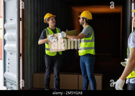 Le travailleur porte une boîte en carton prise dans un conteneur en acier de 40 pieds sur le parking pour camions-remorques à l'entrepôt Banque D'Images