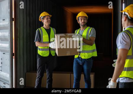 Le travailleur porte une boîte en carton prise dans un conteneur en acier de 40 pieds sur le parking pour camions-remorques à l'entrepôt Banque D'Images