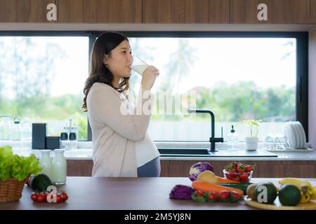 Charmante femme enceinte asiatique qui boit du lait en verre. Une femme attirante a besoin de protéines et de calcium pour son bébé et elle la rend saine et forte. Banque D'Images