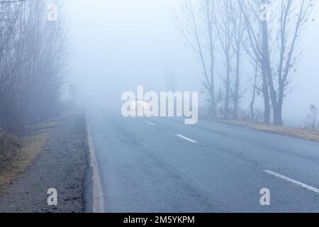 Voiture sur la route dans le brouillard épais par mauvais temps Banque D'Images