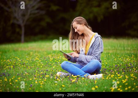 Libre de naviguer où elle le souhaite. une jeune femme utilisant sa tablette numérique dans le parc. Banque D'Images