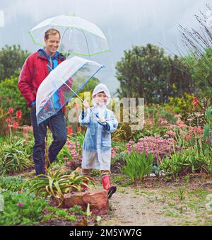 Notre jardin aime la pluie. Photo en longueur d'un père et de son fils marchant dehors sous la pluie. Banque D'Images