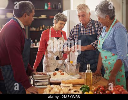 Le début de quelque chose de délicieux. un groupe de personnes âgées qui cuisent dans la cuisine. Banque D'Images