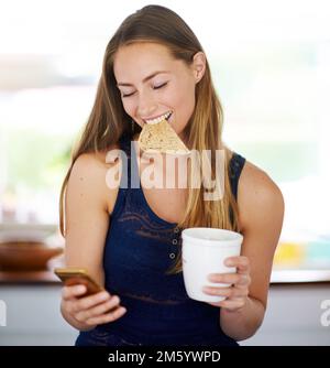Tout le bonheur dépend d'un petit déjeuner tranquille. une femme utilisant son téléphone cellulaire, mangeant des toasts et ayant du café. Banque D'Images