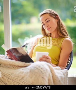 Engrossed dans un excellent livre. une jeune femme lisant un livre à la maison. Banque D'Images