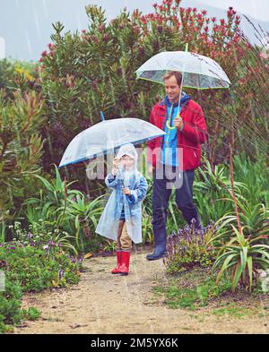 Jours de pluie. Photo en longueur d'un père et de son fils marchant dehors sous la pluie. Banque D'Images