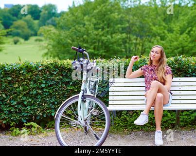 Apprécier la beauté de tout. une jeune femme assise sur un banc pendant qu'elle est en vélo dans le parc. Banque D'Images