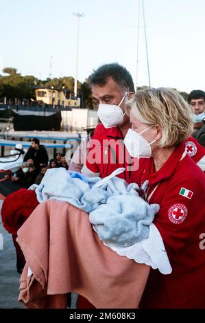 Concetta Gioffré (R), présidente du comité local de la Croix-Rouge, vu avec un nouveau-né. Près de 90 migrants, principalement d'Afghanistan, du Pakistan et d'Iran, ont été sauvés par la Garde côtière italienne et emmenés au port de Roccella Jonica « Porto Delle Grazie ». Un bébé, né il y a trois jours pendant le passage à niveau, un nouveau-né de 11 jours et un bébé de cinq mois étaient également à bord. Des membres de la Croix-Rouge, des médecins sans frontières et du personnel sanitaire ont aidé les bébés, leurs familles et d'autres migrants. Banque D'Images