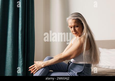 Une femme âgée triste et attentionnés, assise dans la chambre et regardant vers le bas Banque D'Images