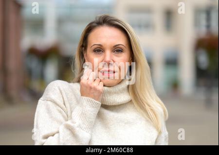 Jolie blonde d'âge moyen, femme tenant son col de cygne avec ses mains dans une ville Banque D'Images